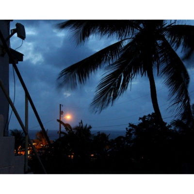 Photograph of a porch in the Caribbean at dusk with a palm frond and ocean in the background.